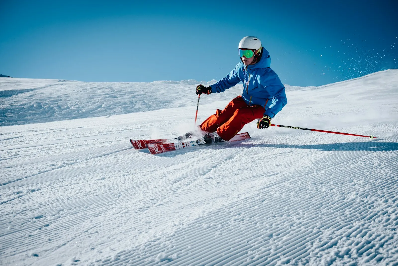 A skier in a blue jacket carving down a groomed run