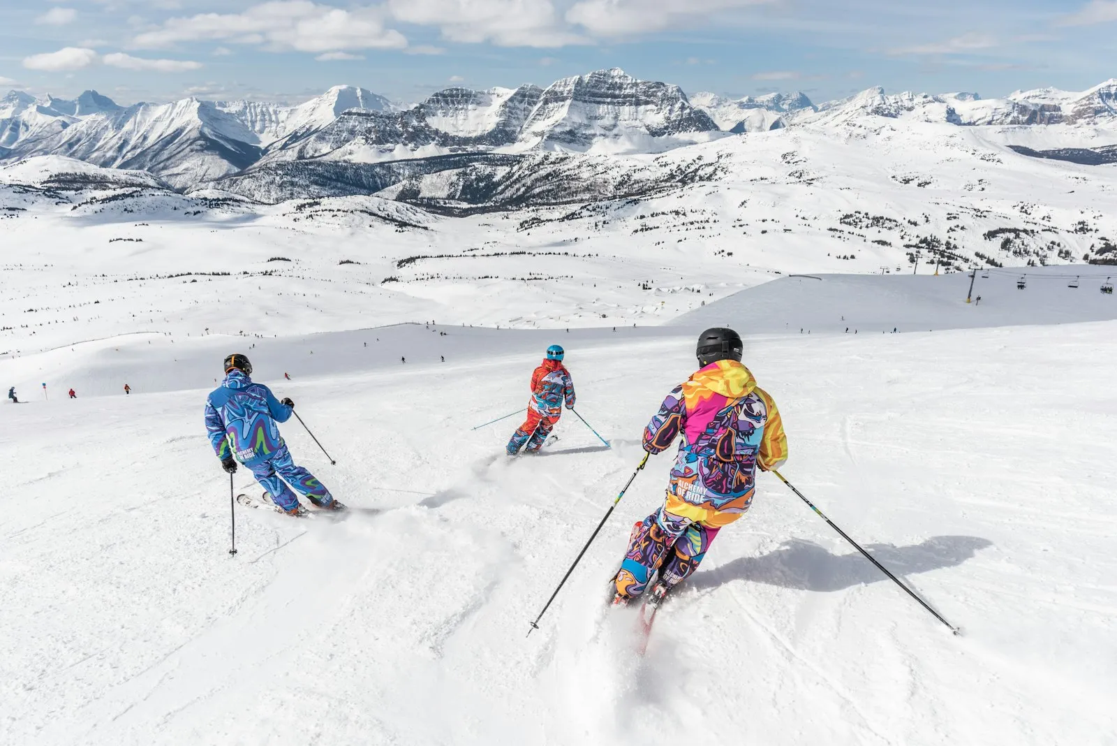 Three skiers heading down a wide slope toward distant mountains
